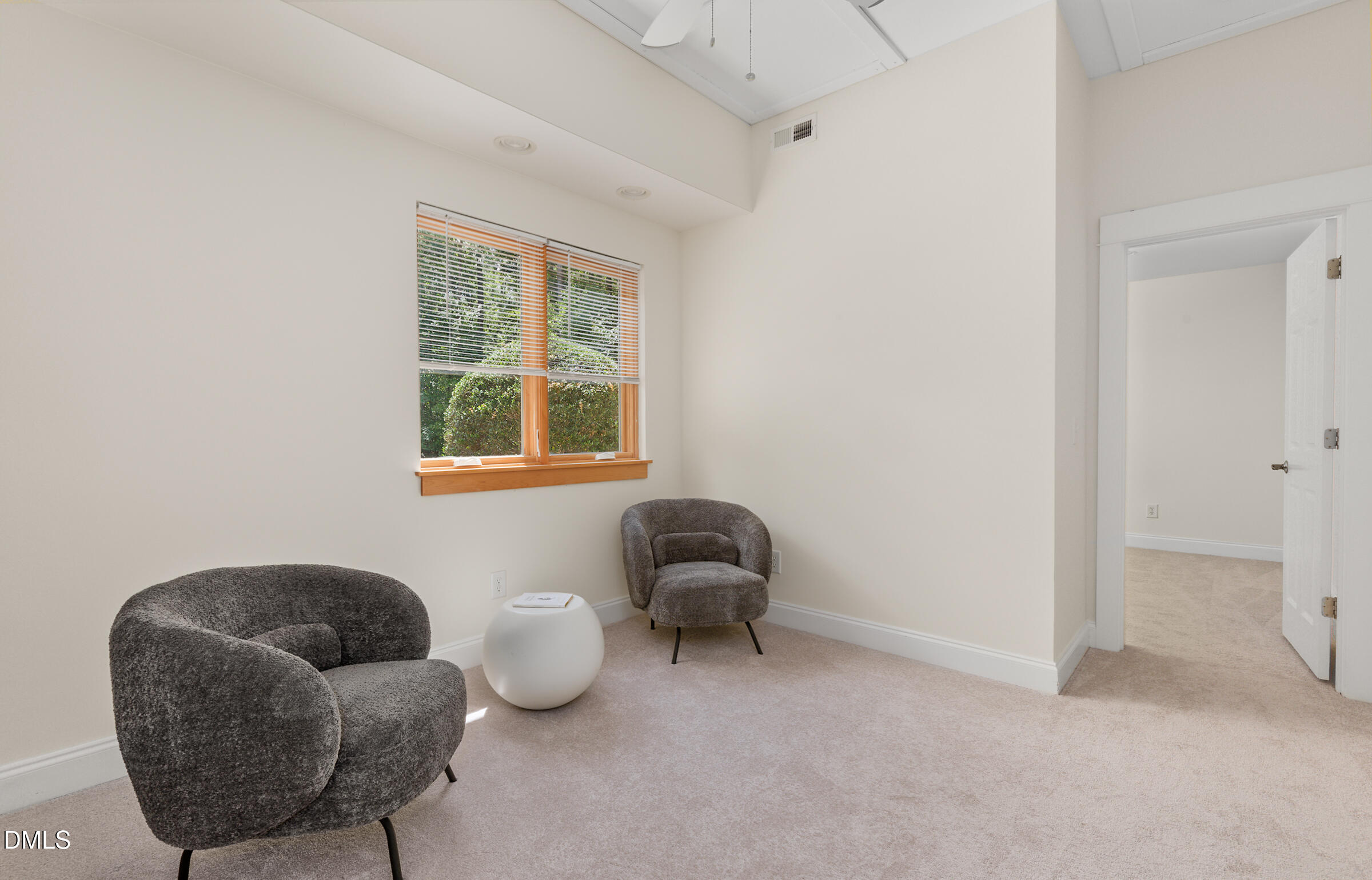Sitting room with two gray lounge chairs, a white round table, and a window overlooking greenery.