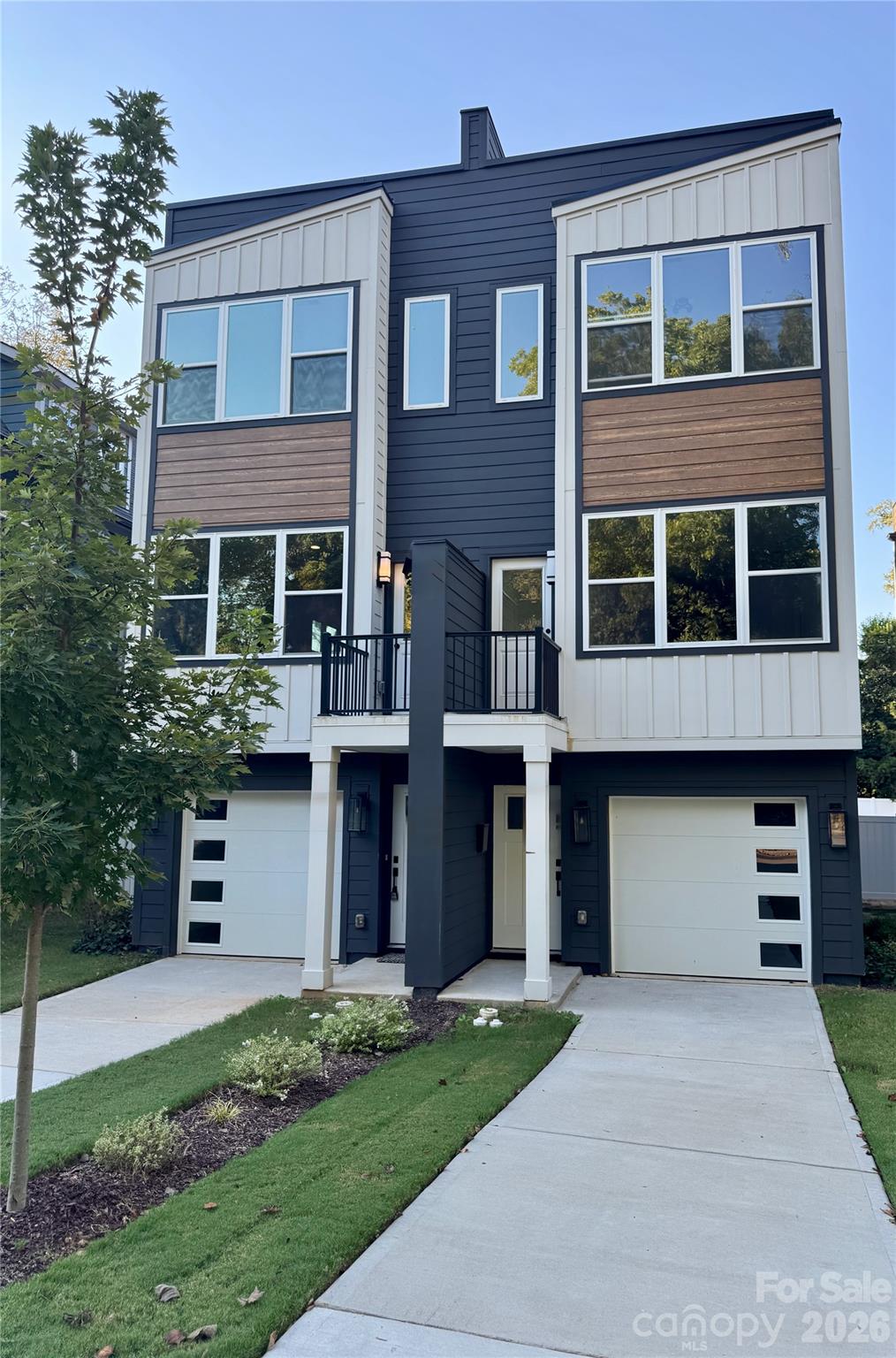 Modern navy-and-white multi-story home with two garages, a small balcony, and landscaped front lawn.