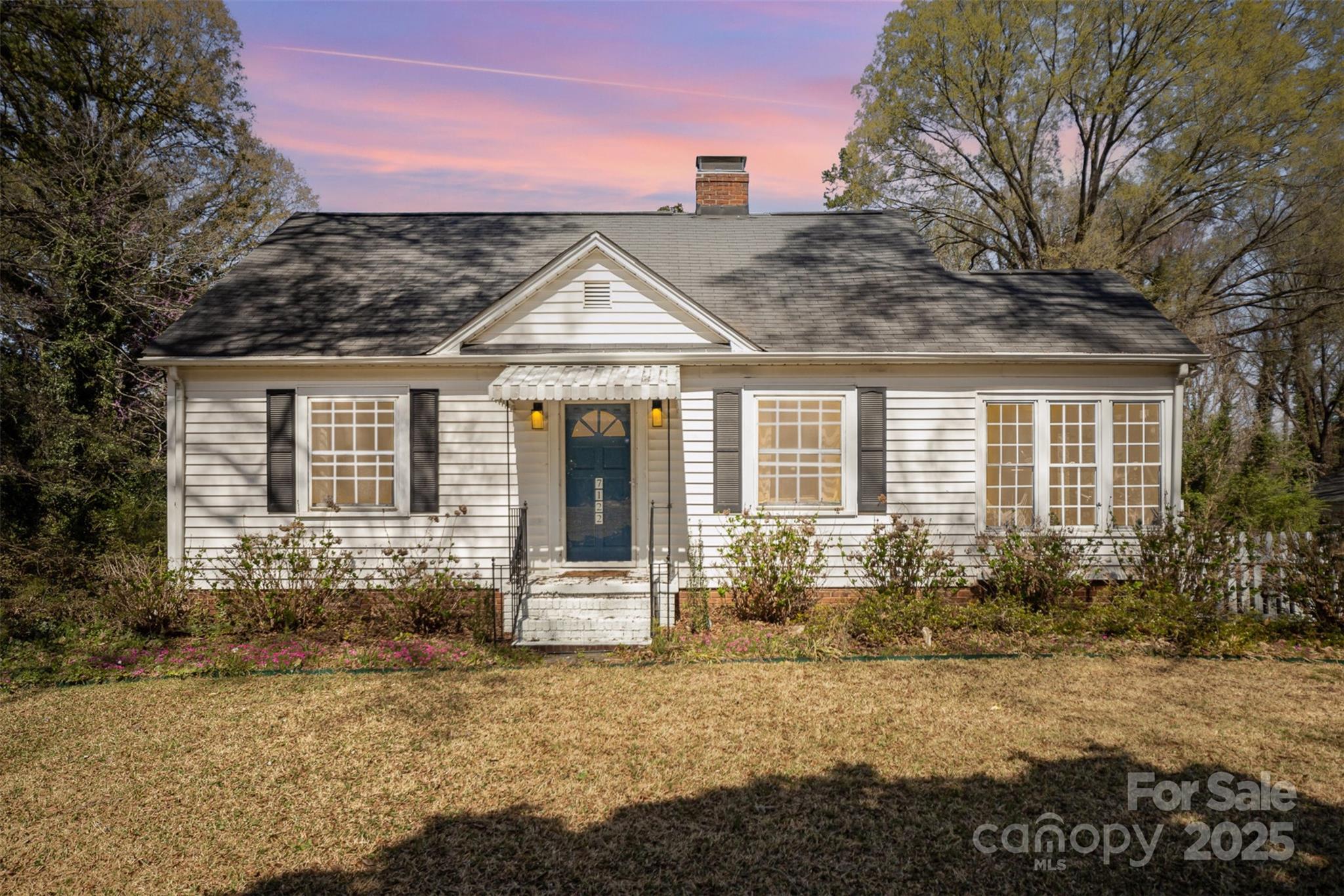 White one-story house with blue front door, black shutters, and pink sunset sky.
