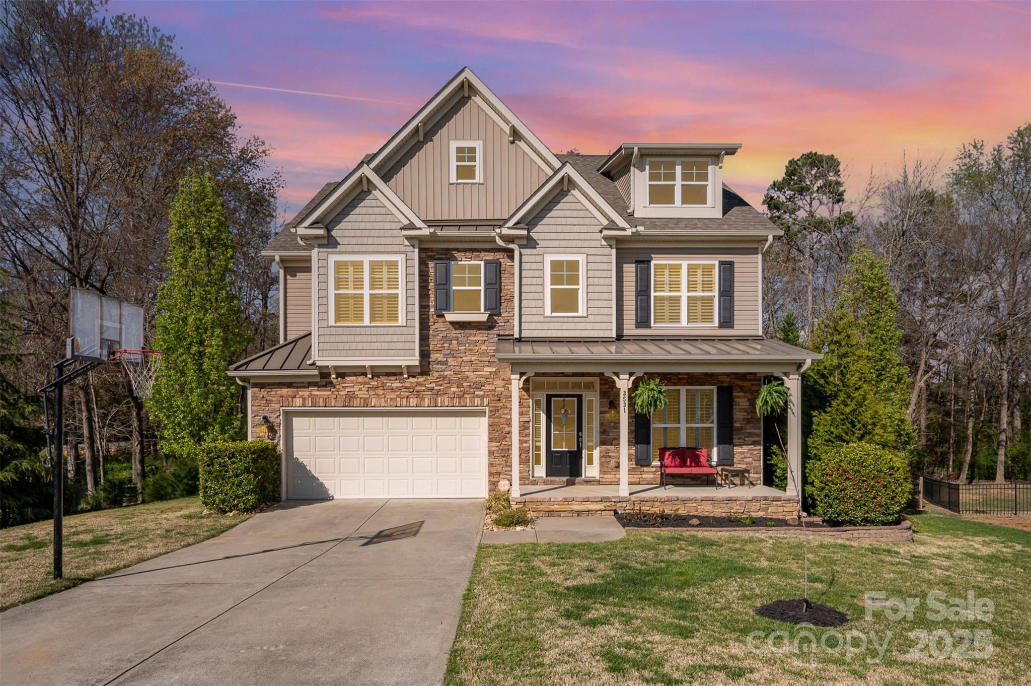 Two-story house with stone accents, a covered porch, and a basketball hoop beside the driveway.