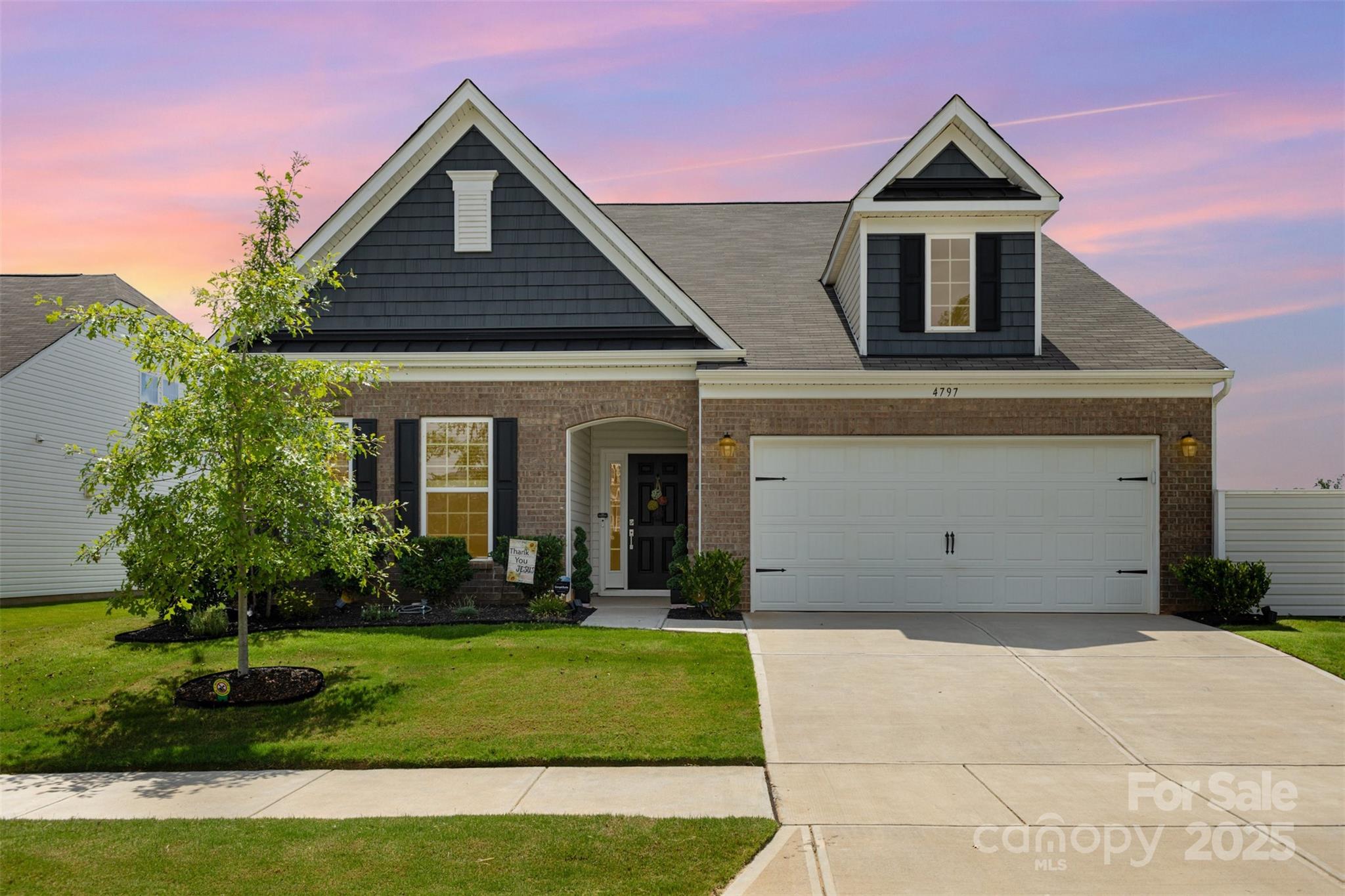 Brick two-story home with dark gables, white trim, a two-car garage, and a pink dusk sky.
