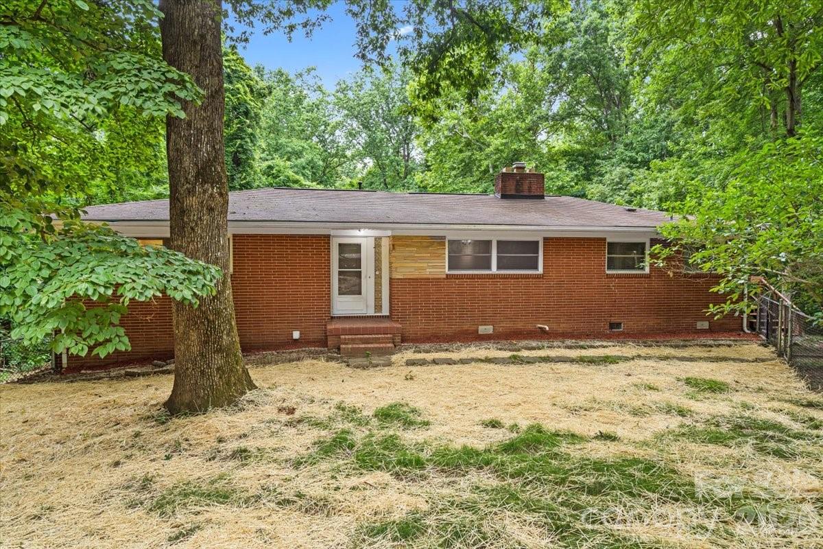 Single-story brick home with a low roof, centered entry, and wooded surroundings.