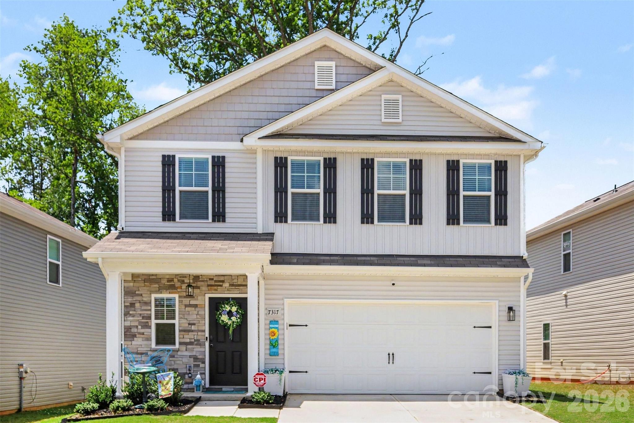 Two-story white house with black shutters, stone porch, and a two-car garage.