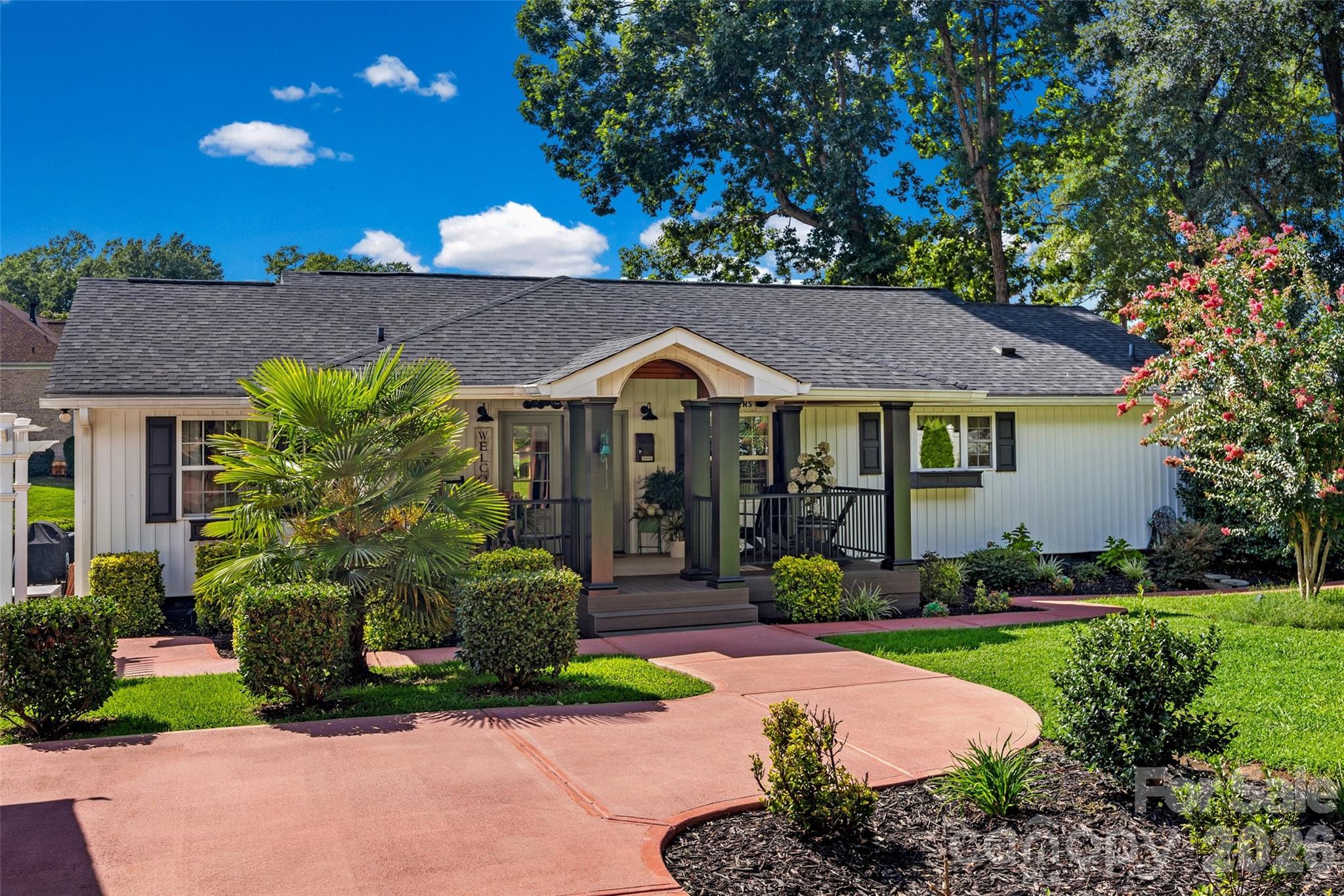 Single-story white house with a columned porch, curved driveway, and landscaped front yard.