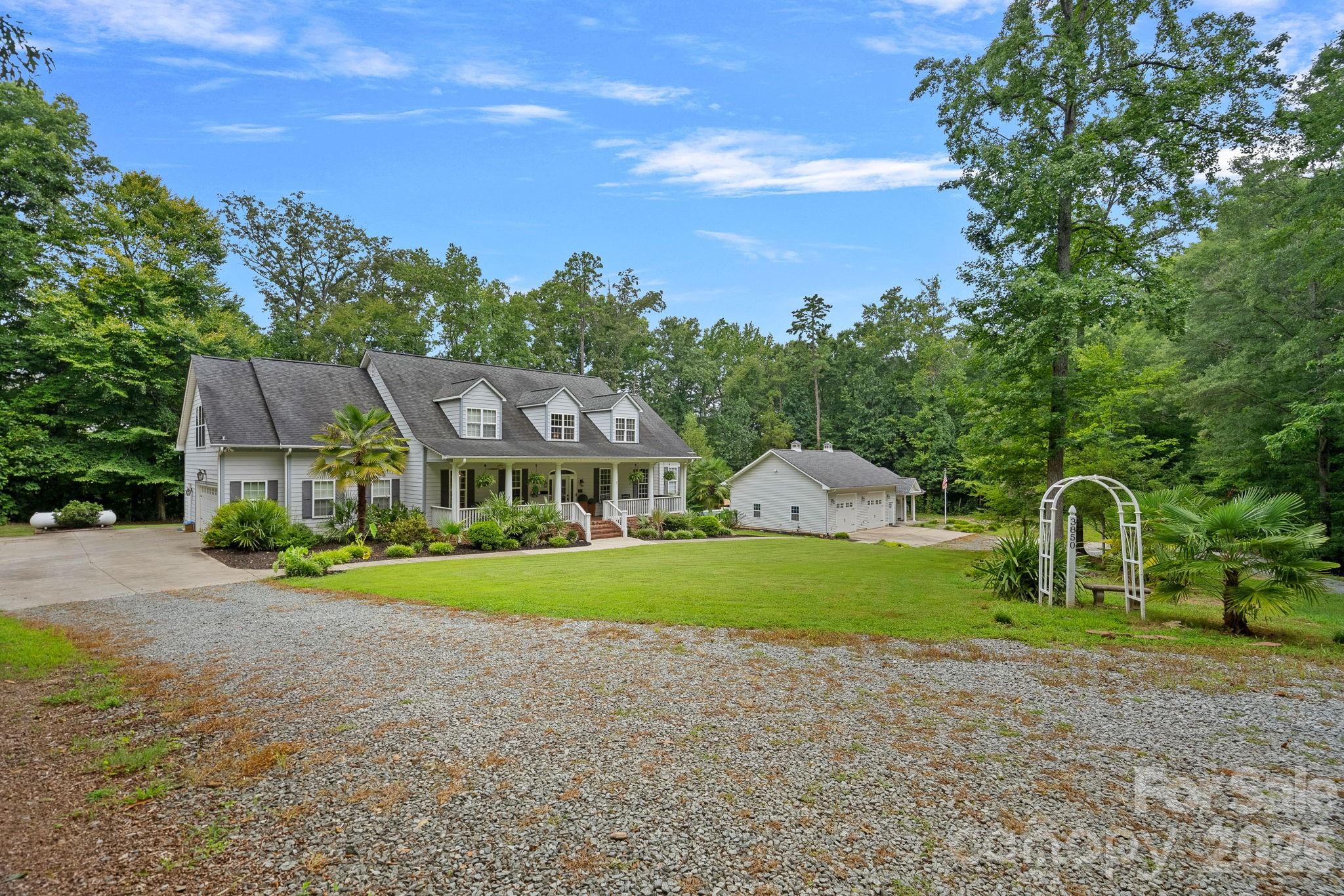 Gray two-story home with a covered porch, detached garage, gravel drive, and white garden arbor.