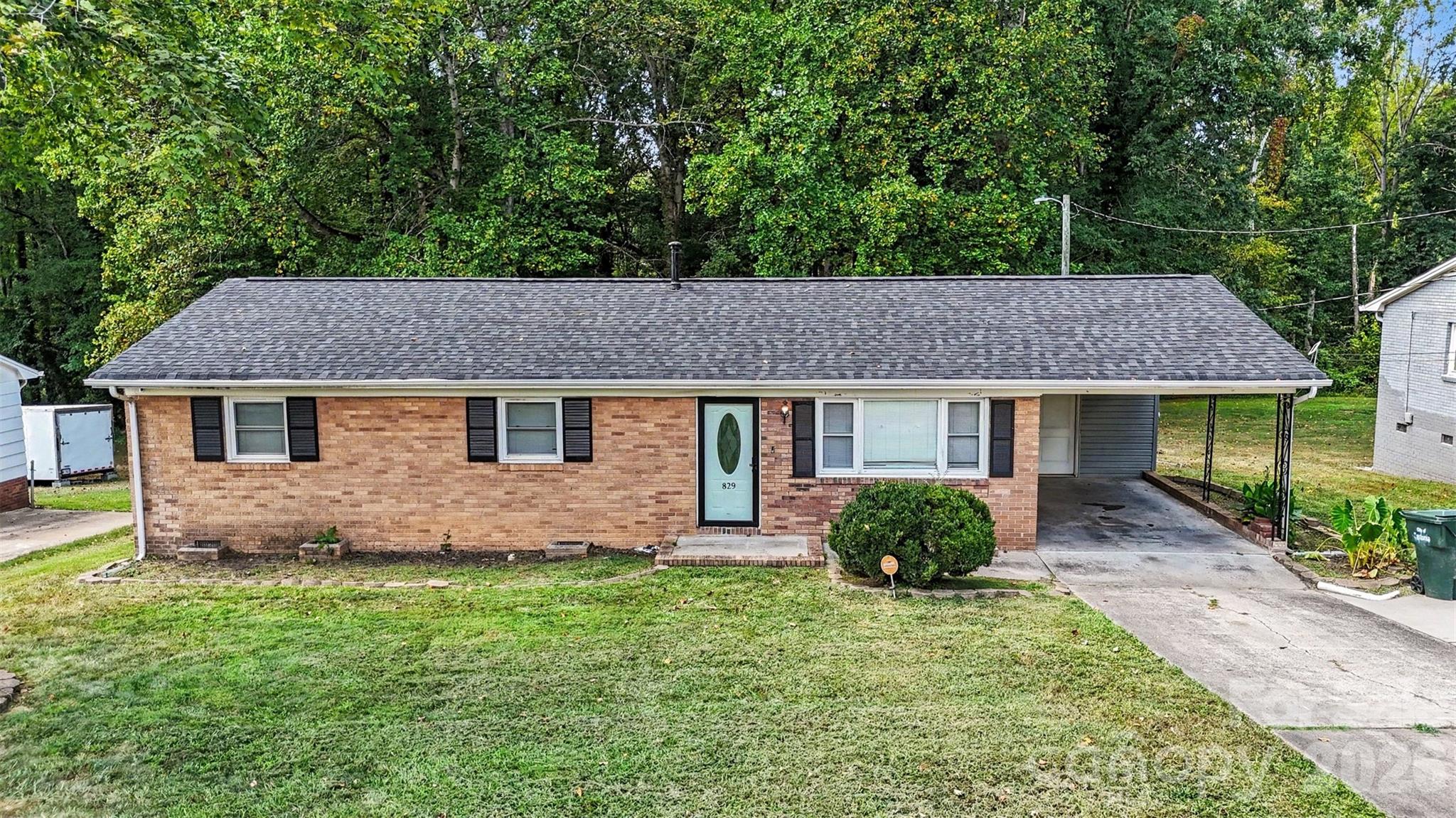 Brick ranch house with a pale green front door, black shutters, and attached carport.