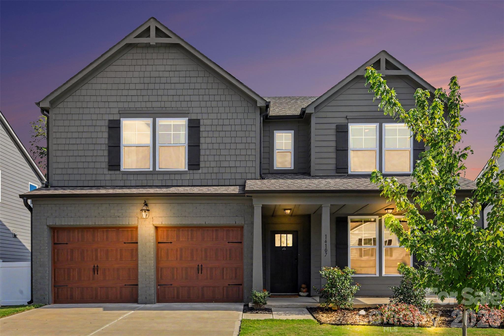 Gray two-story home with twin wooden garage doors and a covered porch at dusk.