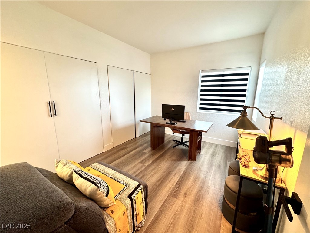 Furnished home office with a desk, computer, gray sofa, built-in closets, and striped window blinds.