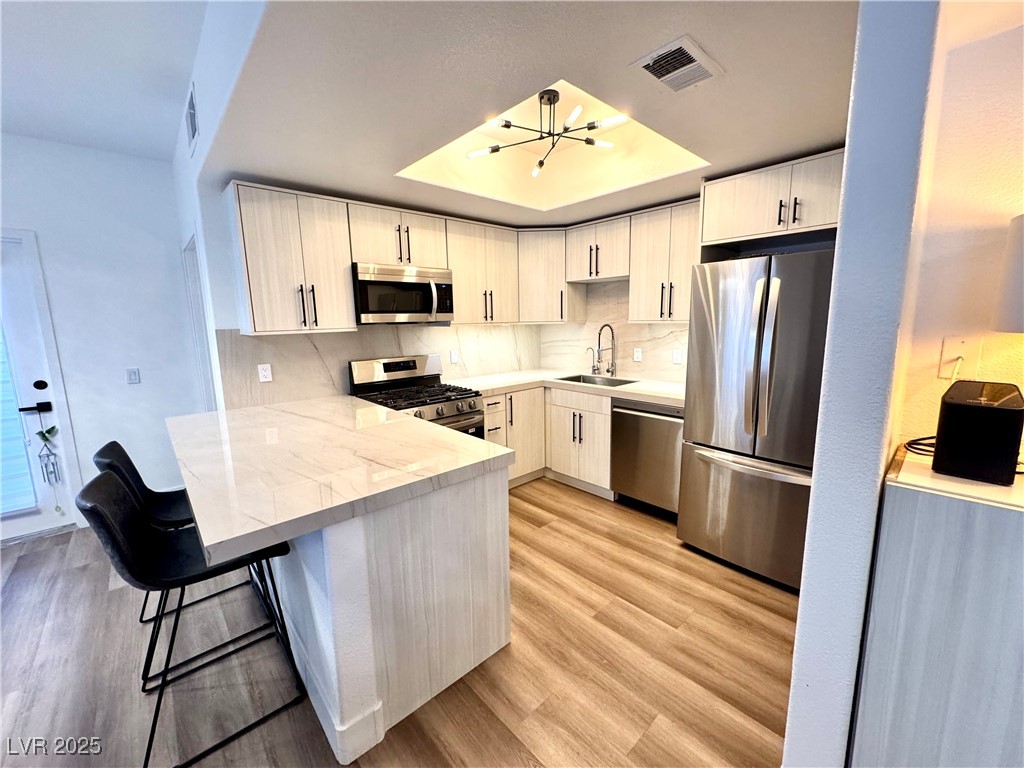 Modern kitchen with a marble-look peninsula, light wood cabinets, and stainless steel appliances.
