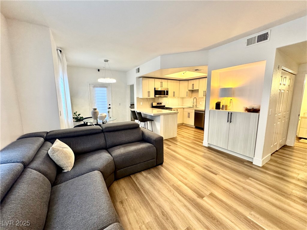 Open-plan living room and kitchen with a dark sectional, breakfast bar, and light wood flooring.