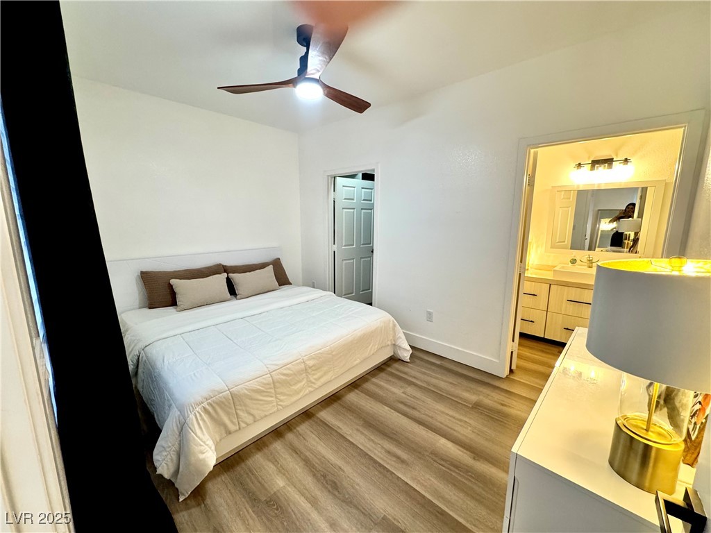 Bedroom with a white bed, ceiling fan, wood-look flooring, and an open doorway to the bathroom.