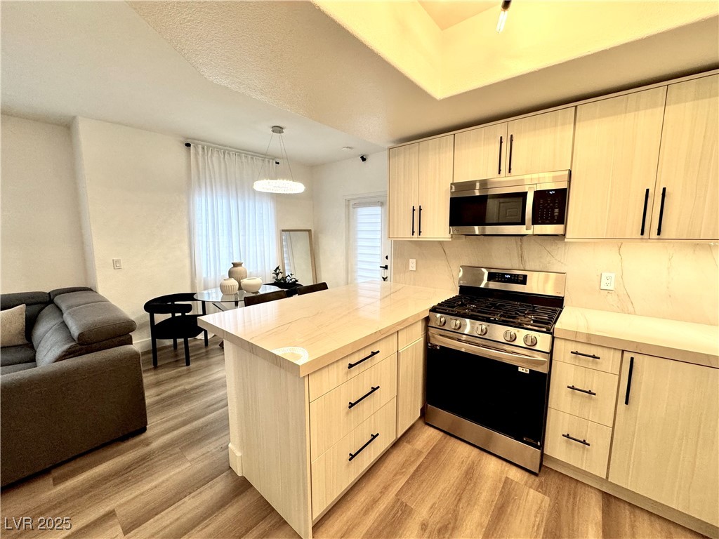 Open-plan kitchen with a large island, light wood cabinets, and stainless steel appliances.