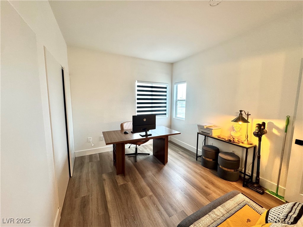 Furnished home office with a wooden desk, monitor, striped blind, and lit console table.