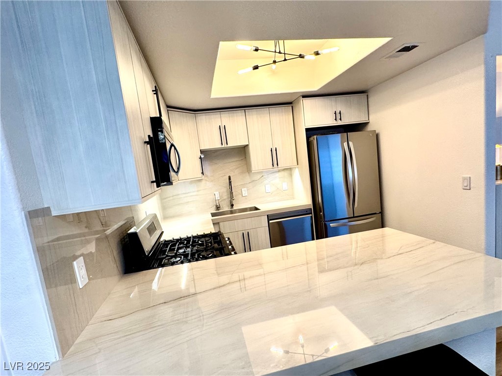 Modern kitchen with a large marble-patterned island, pale wood cabinets, and stainless steel appliances.