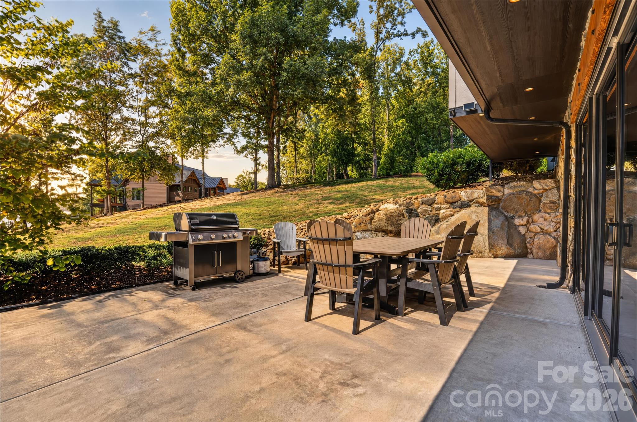 Outdoor patio with a dining set, stainless steel grill, and stone retaining wall.
