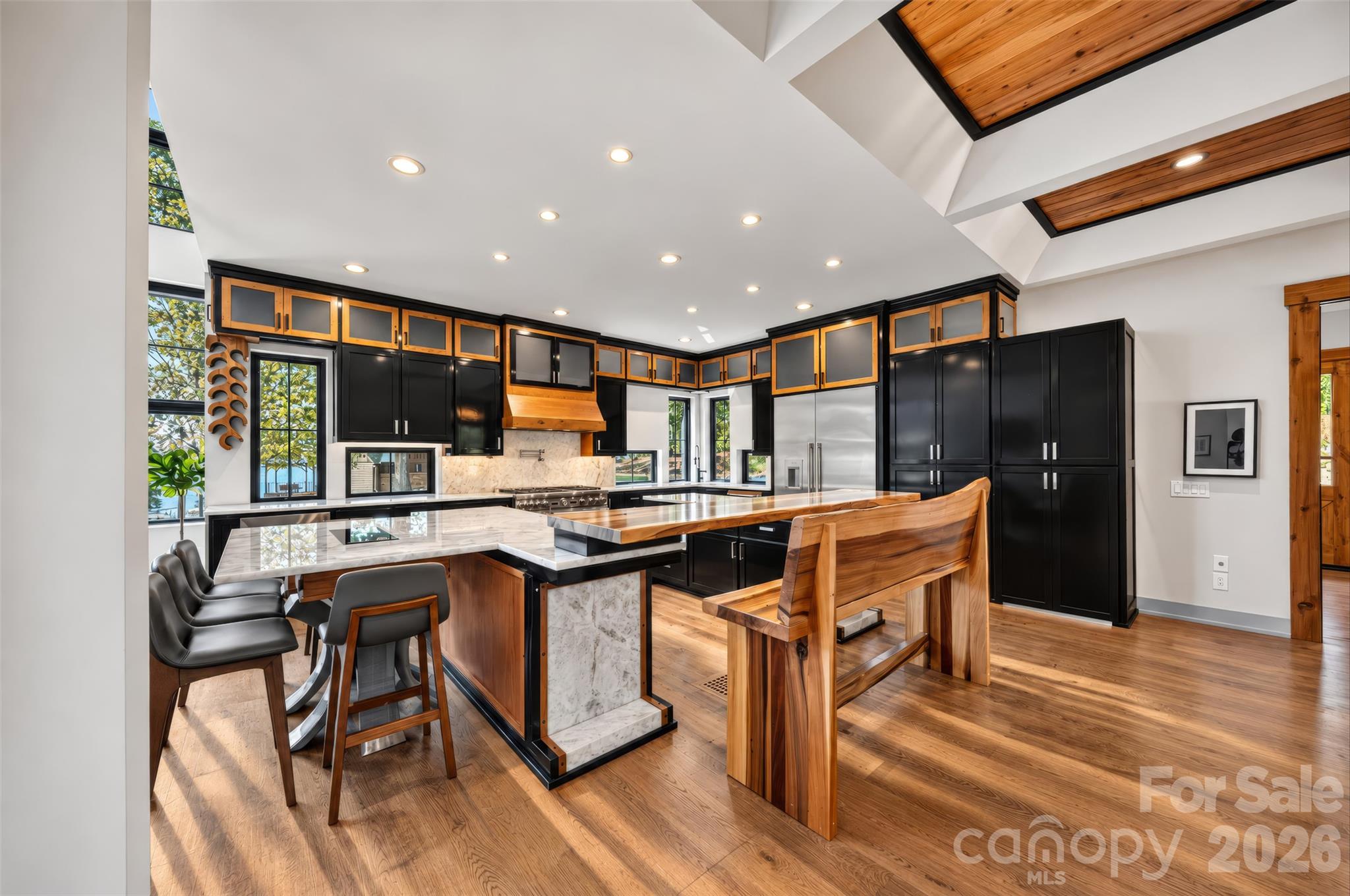 Kitchen with black and wood cabinetry, marble counters, a large island, and a vaulted wood-accented ceiling.