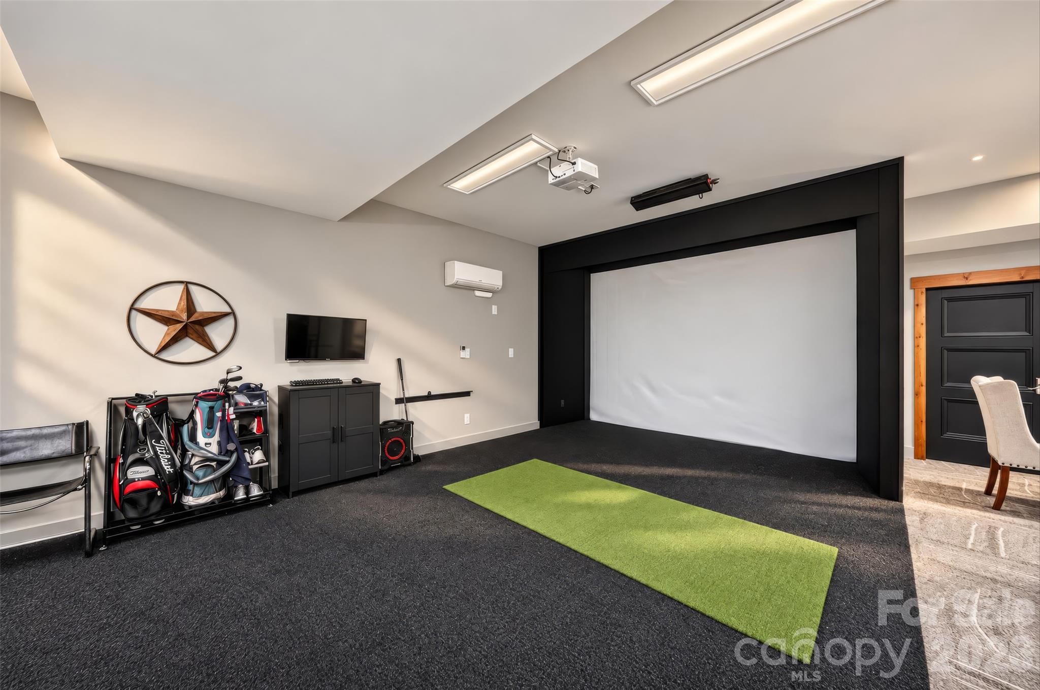 Recreation room with a large projection screen, golf clubs, and a putting mat.
