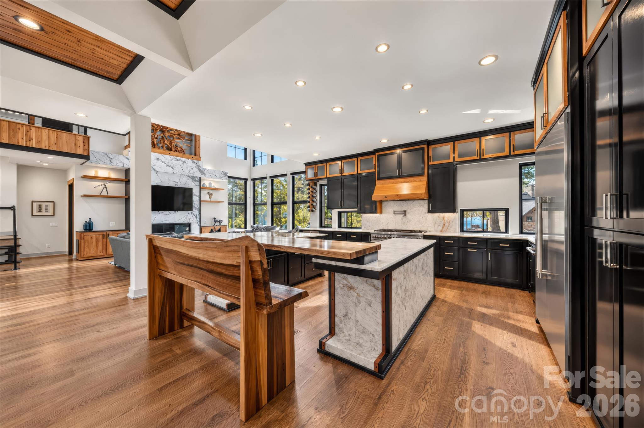Open-plan kitchen with a marble island, black and wood cabinetry, and a built-in wood dining counter.