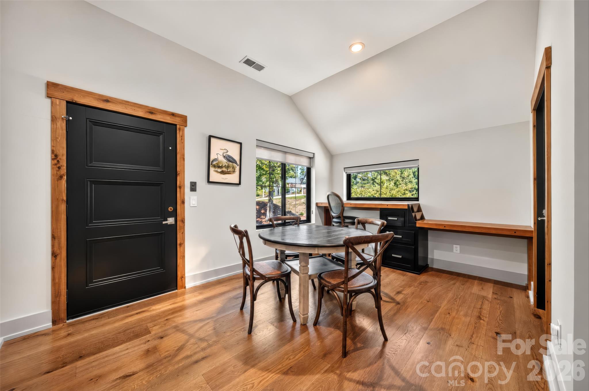 Dining nook with round table, built-in desk, hardwood floors, and a wood-trimmed black door.