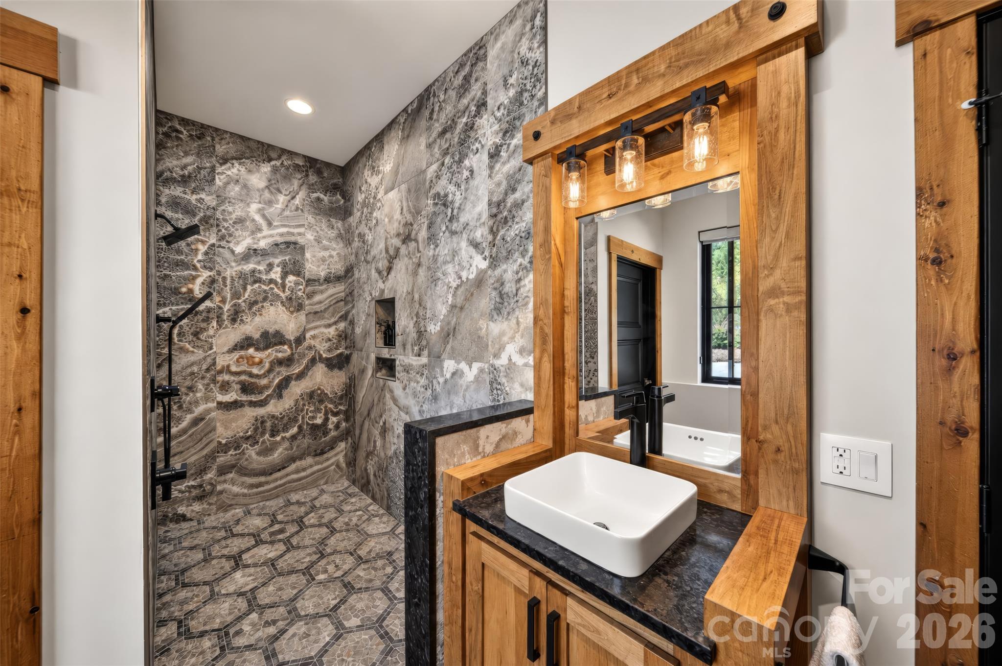 Bathroom with a patterned stone walk-in shower and a wood vanity with a white vessel sink.