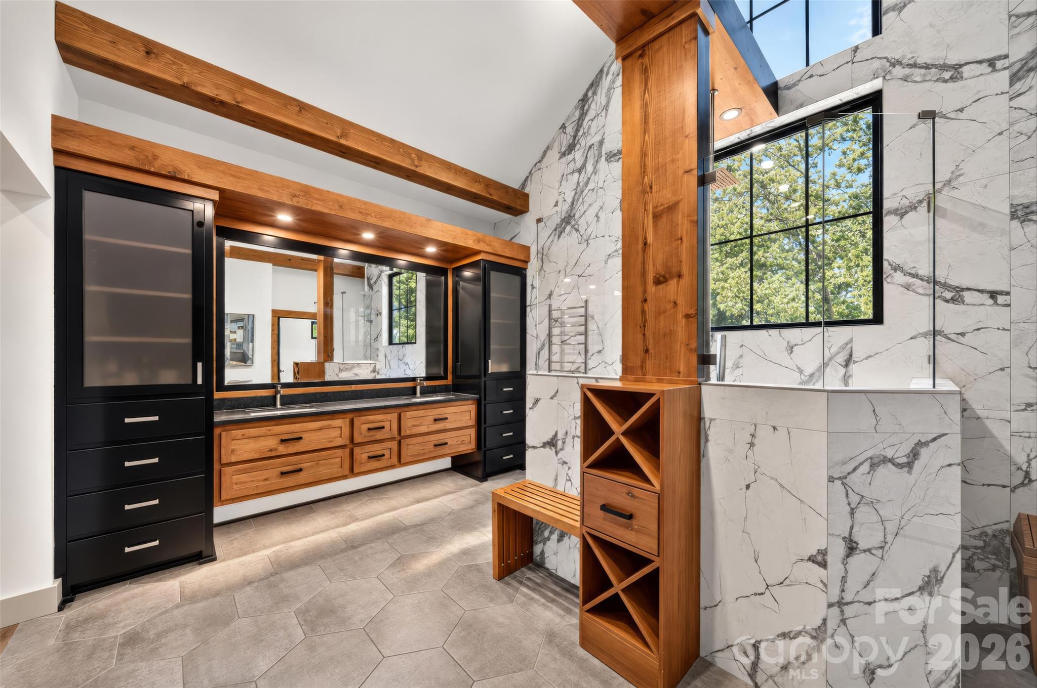 Modern bathroom with a timber-beam ceiling, wood vanity, marble-patterned walls, and large window.