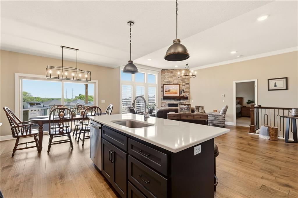 Open-plan kitchen with a large dark island, wood floors, dining table, and stone fireplace.