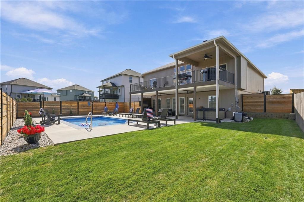 Home’s rear exterior with a covered balcony, fenced lawn, and swimming pool.