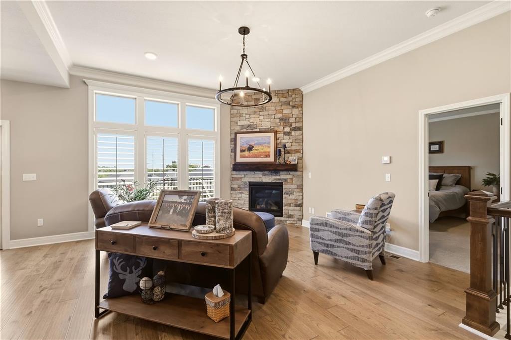 Staged living room with a stone fireplace, tall shuttered windows, and light wood floors.