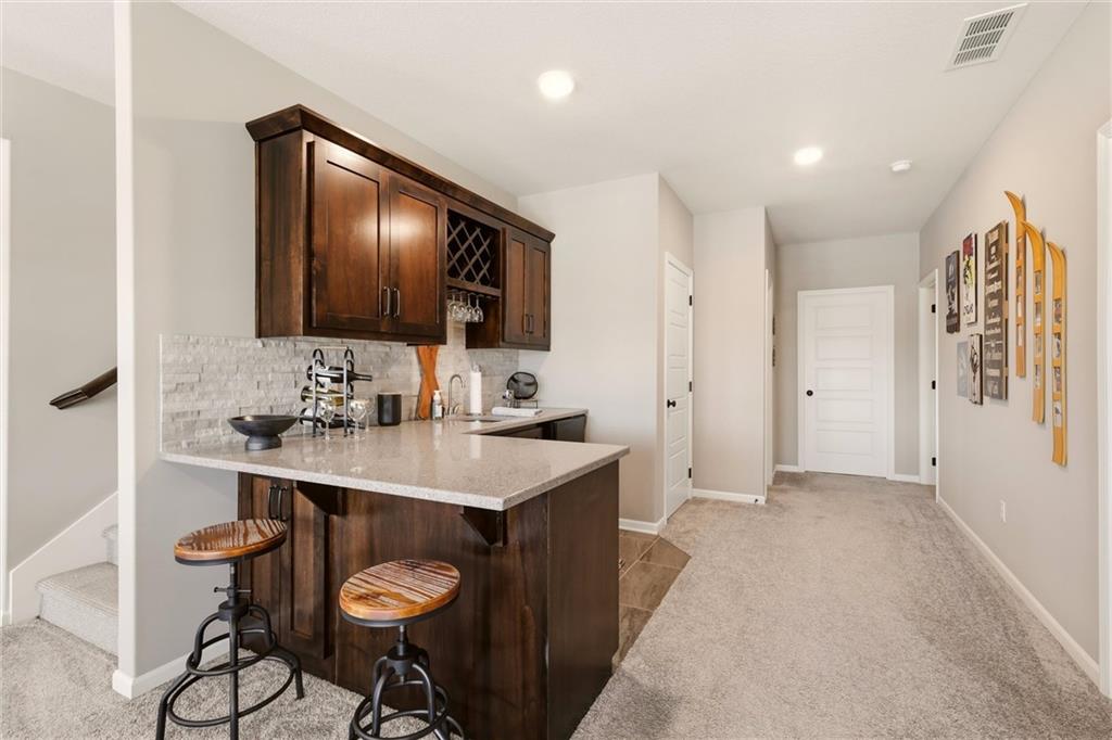 Hallway wet bar with dark wood cabinetry, stone counter, and two stools.