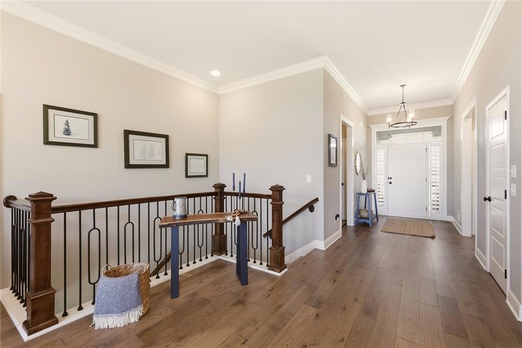 Upstairs hallway with warm wood floors, an iron railing, and the front entry door.