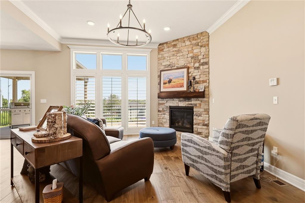 Living room with a stone fireplace, tall shuttered windows, wood floors, and a chandelier.