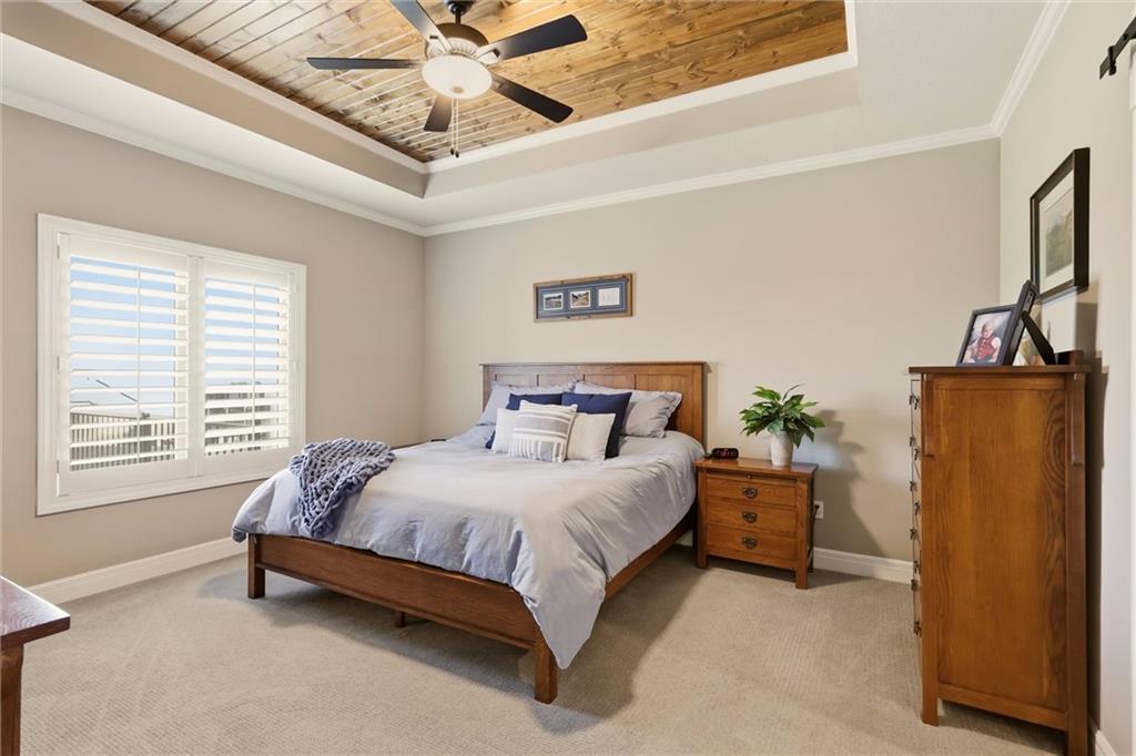 Bedroom with a wood bed, plantation shutters, and a wood-plank tray ceiling.