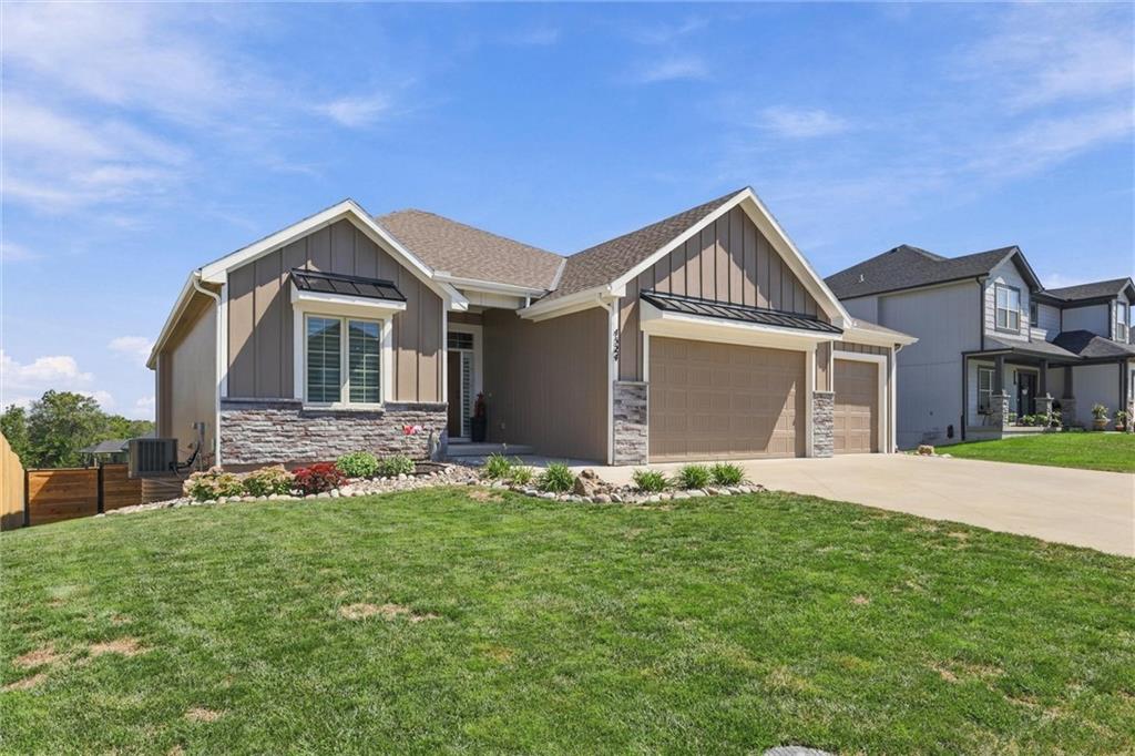 Gray single-story home with stone accents, three-car garage, landscaped flower bed, and broad lawn.
