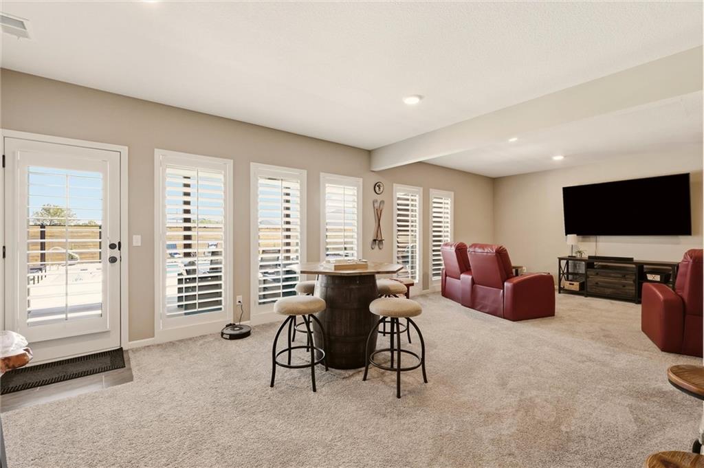 Furnished family room with shuttered windows, a barrel table and stools, red leather chairs, and a wall-mounted TV.