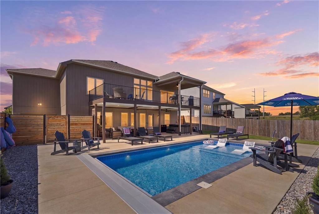 Backyard pool beside a two-story home, with a fenced patio and upper-level deck at dusk.