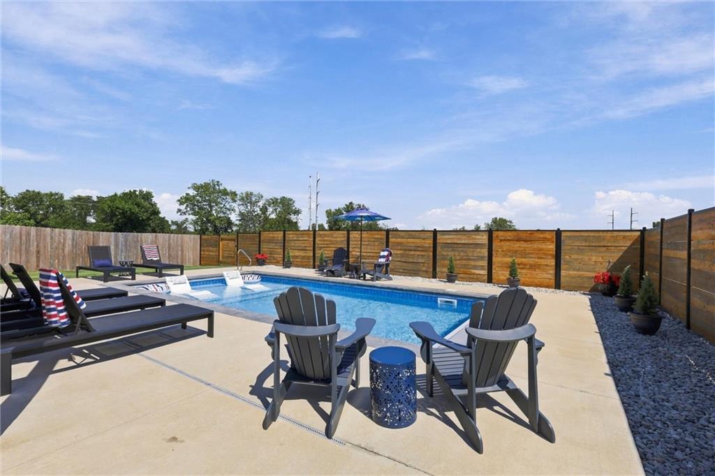 Backyard swimming pool with lounge chairs, Adirondack chairs, and a wooden privacy fence.