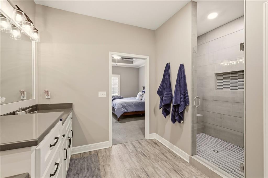 Bathroom with a glass-enclosed gray tile shower and vanity, opening to a bedroom.