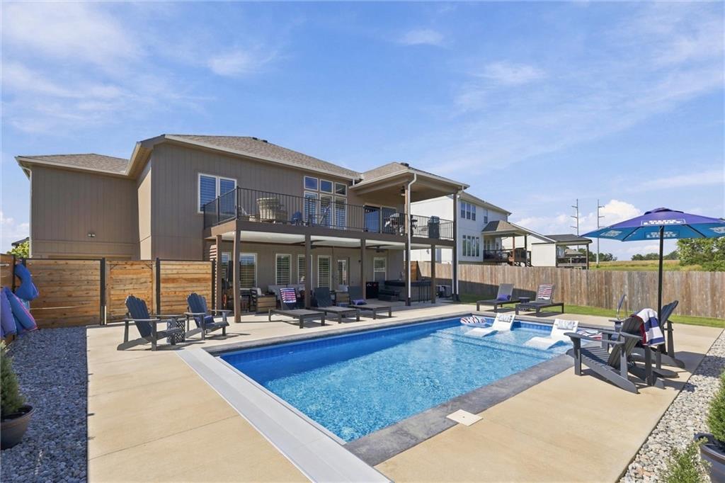 Home’s rear patio with a swimming pool, lounge chairs, and an elevated covered deck.