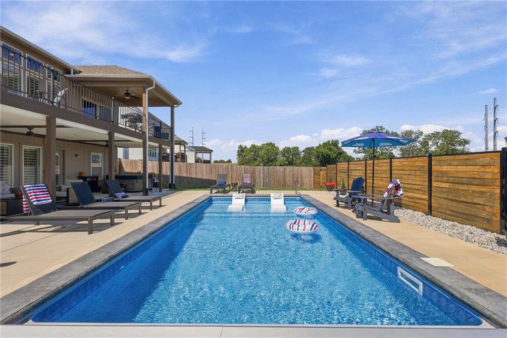 Outdoor pool beside a two-story home, with a covered deck and wooden privacy fence.