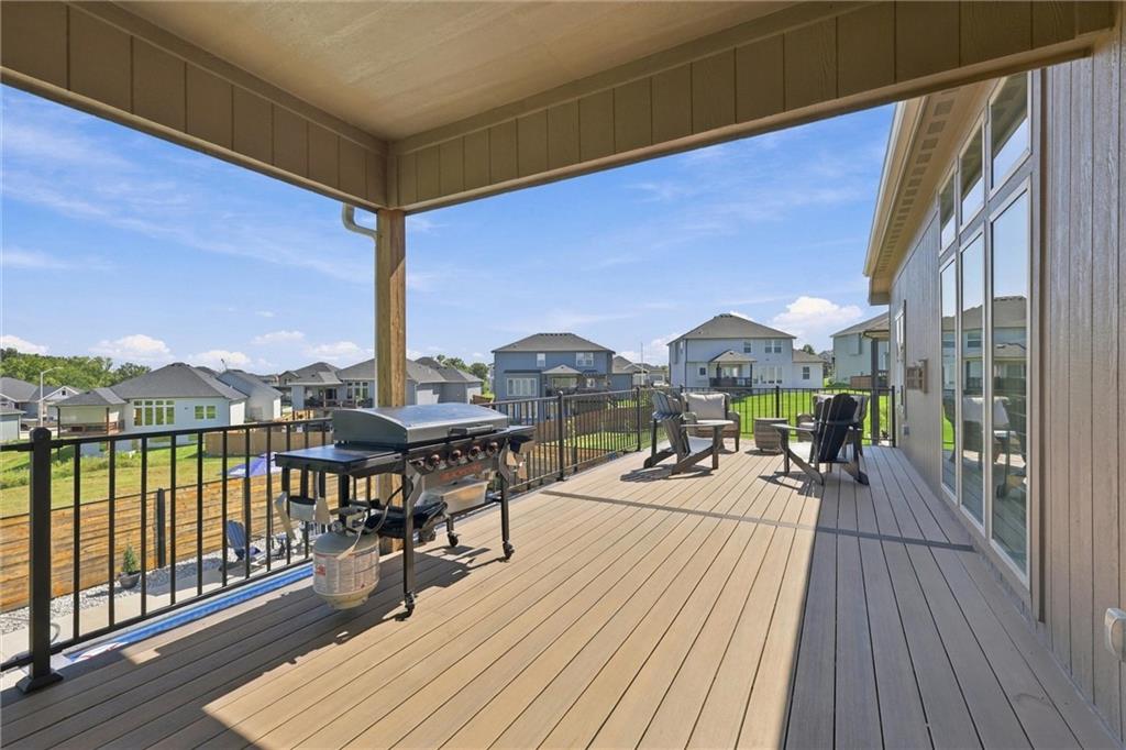 Covered deck with a gas grill and outdoor seating overlooking neighboring homes.