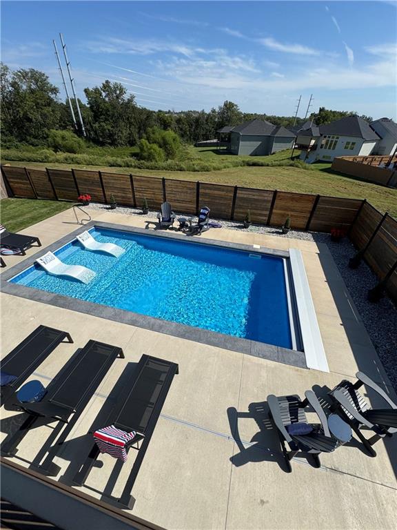 Backyard swimming pool with in-water loungers and a paved patio with black chairs.