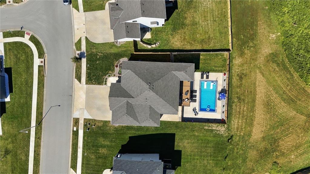 Aerial view of a home with a rectangular backyard pool, lawn, and driveway.