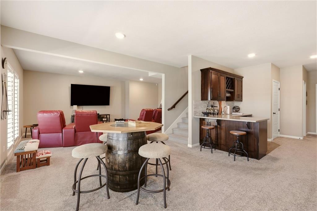 Open living and dining area with red leather recliners, barrel table, kitchen island, and staircase.