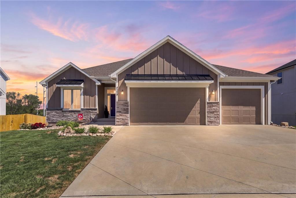 Gray home with stone accents and a three-car garage beneath a pink sunset sky.
