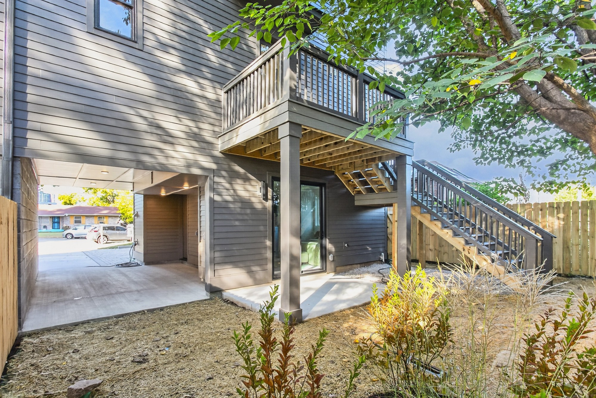 Gray-sided home with an elevated deck and stairs above a covered parking area and fenced yard.