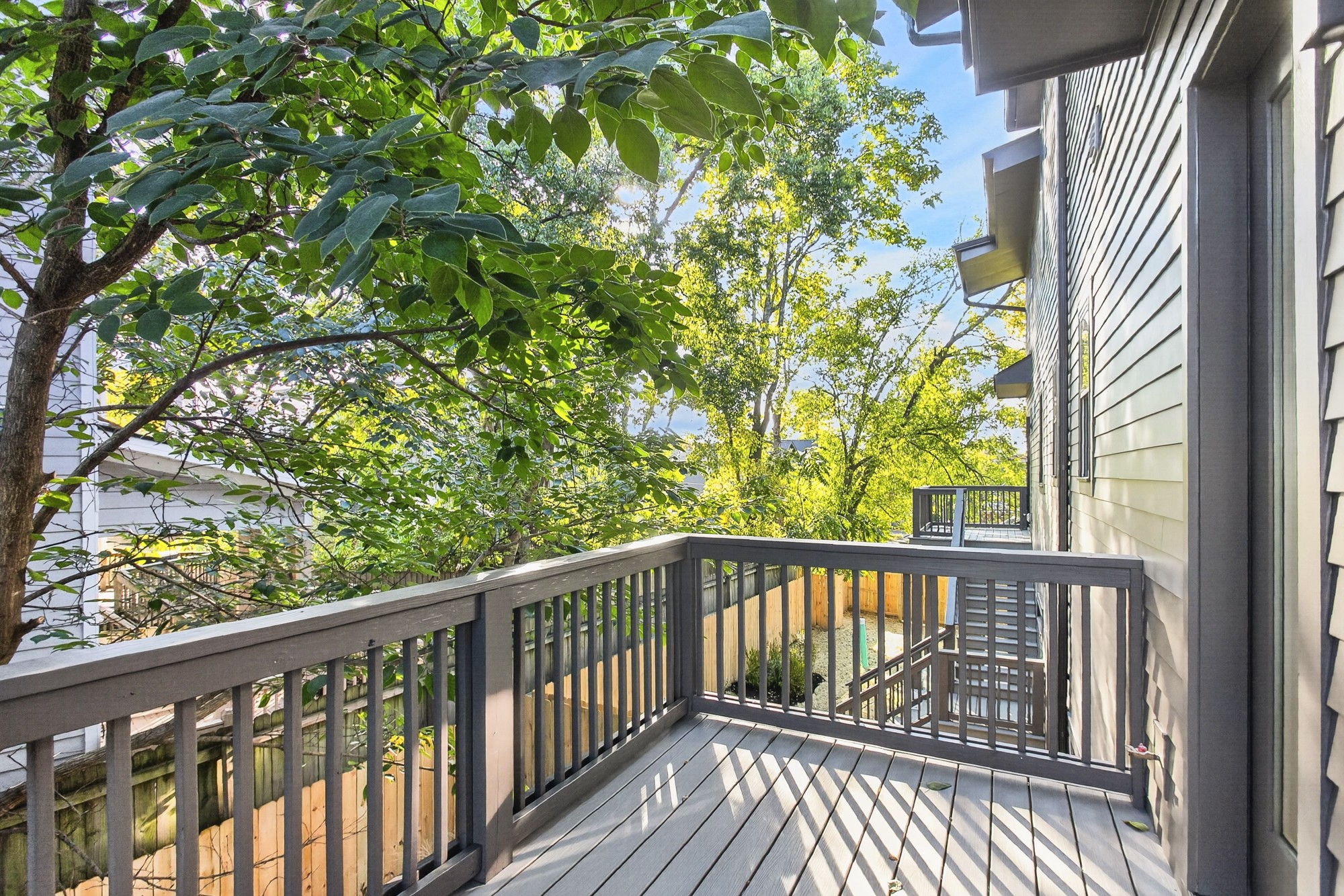 Raised gray side deck with railings and stairs, surrounded by leafy trees.