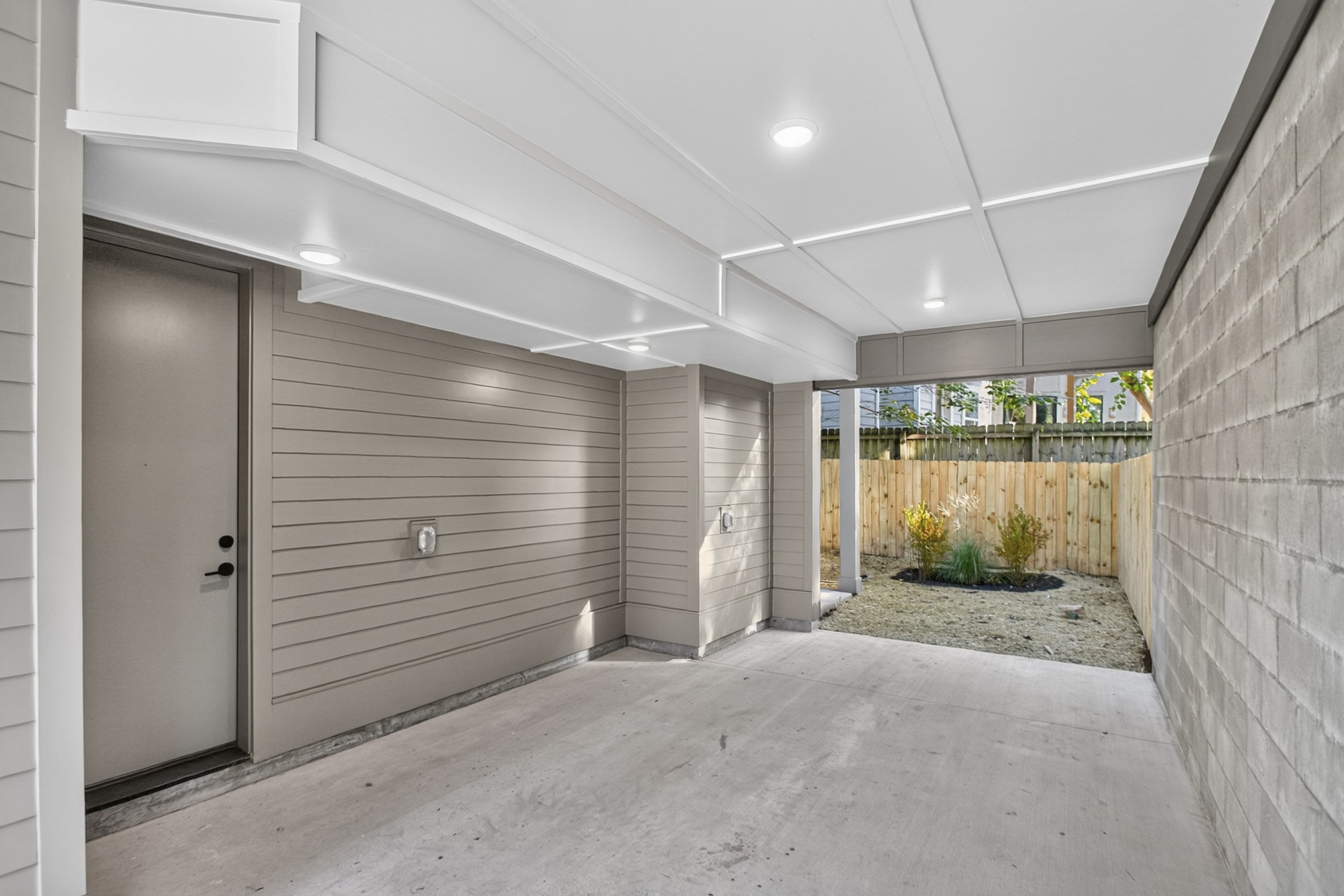 Covered carport with a concrete floor, side door, and fenced yard at the far end.