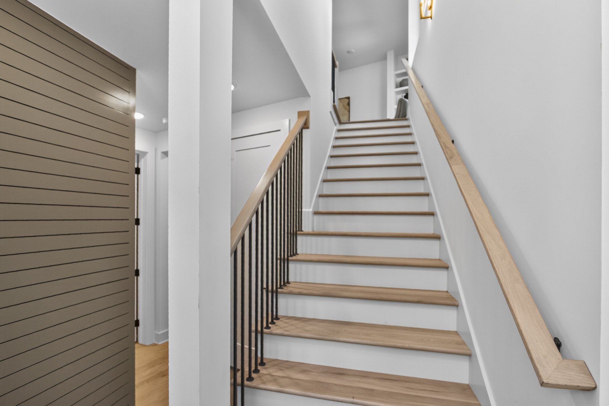 Interior staircase with light wood treads and handrails, black metal balusters, and a dark paneled door.