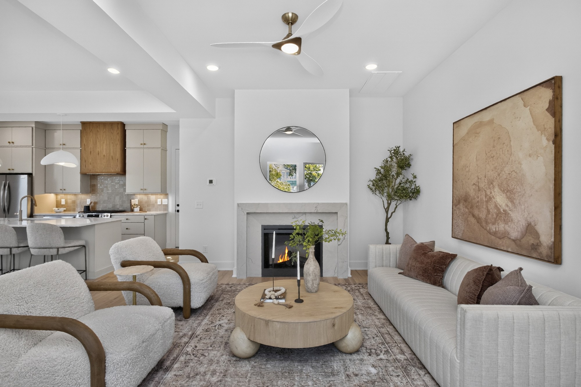 Furnished living room with a marble-surround fireplace, textured white seating, and an open kitchen.