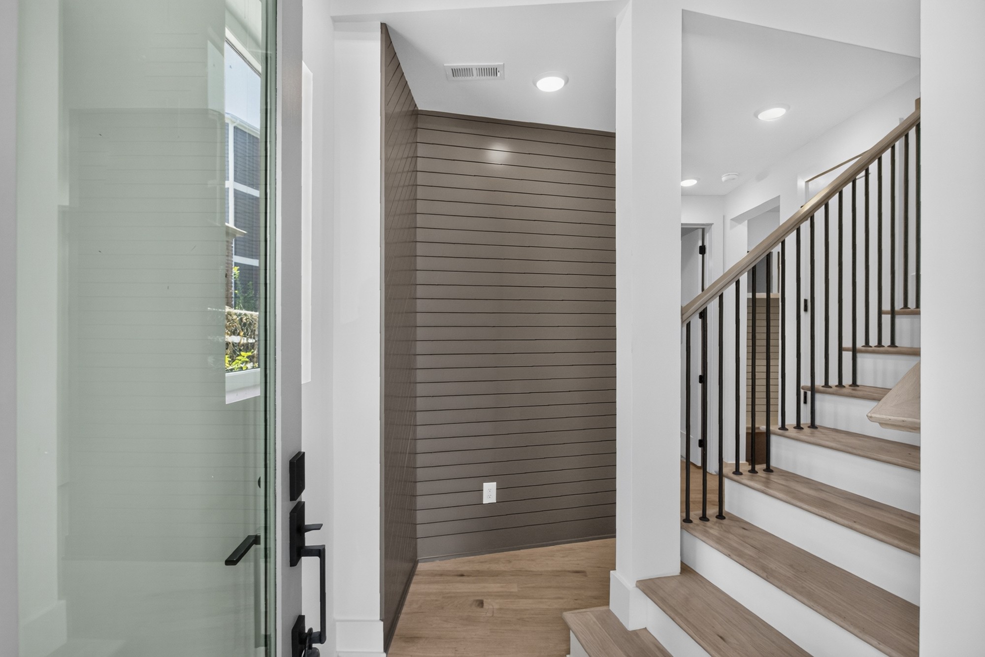 Entry foyer with a glass front door, paneled accent wall, wood floor, and open staircase.